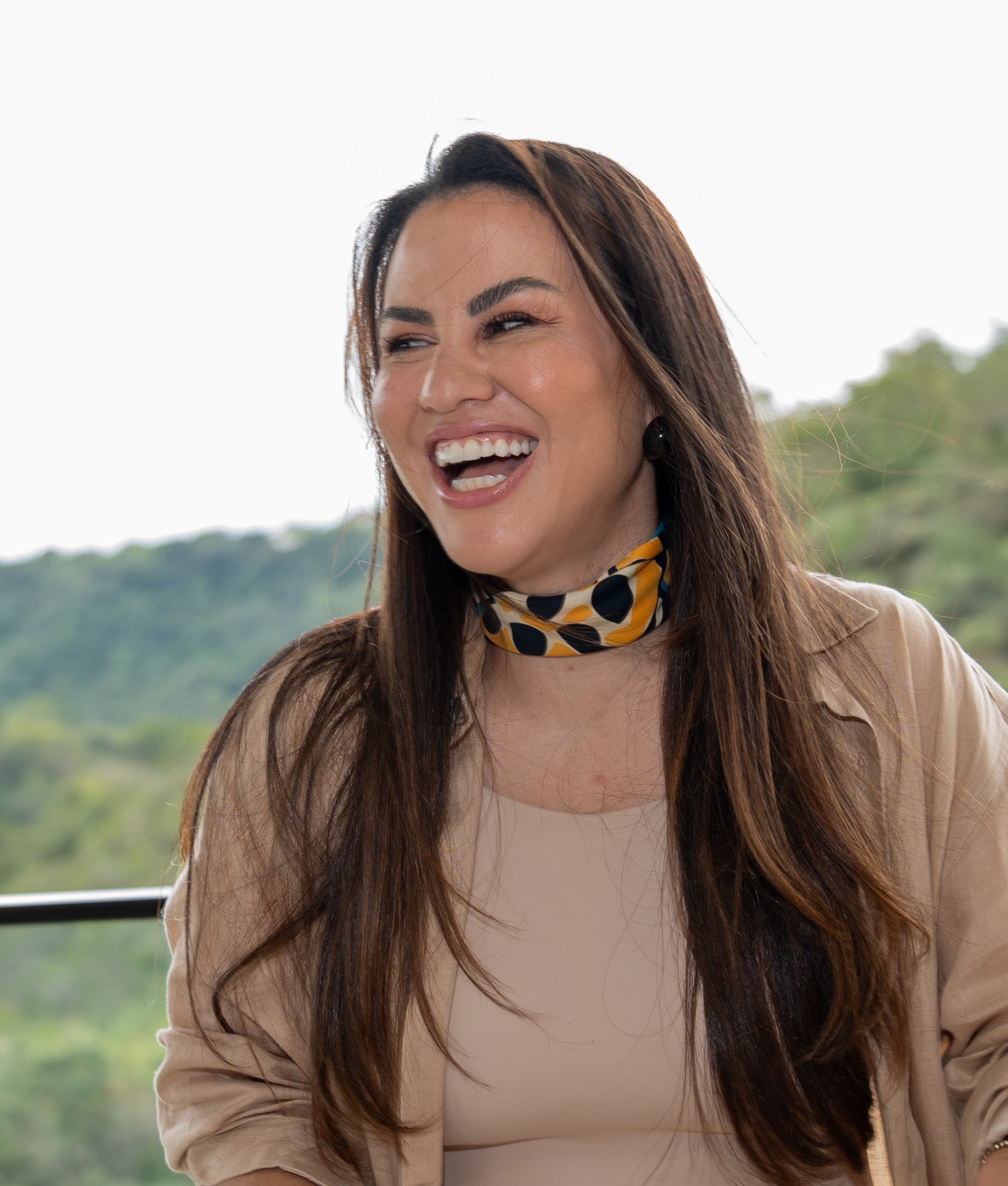 Fundadora da SENS sorrindo, de blazer bege e lenço estampado.